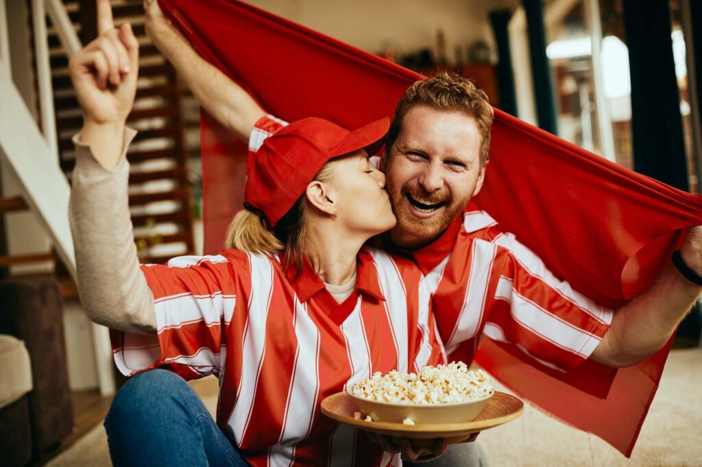 Happy sports fan and his girlfriend cheering while watching championship on TV at home.